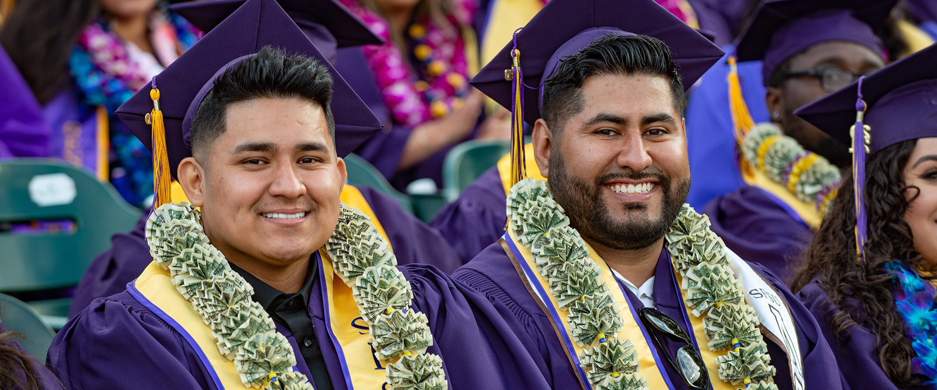Business graduates wearing money leis and regalia at Commencement