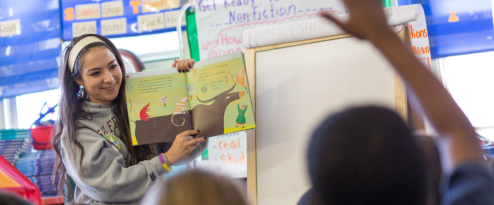 Teacher reads a book to a classroom of children. A student raises his hand.
