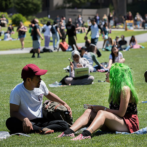 Students on the campus lawn. One has green hair.