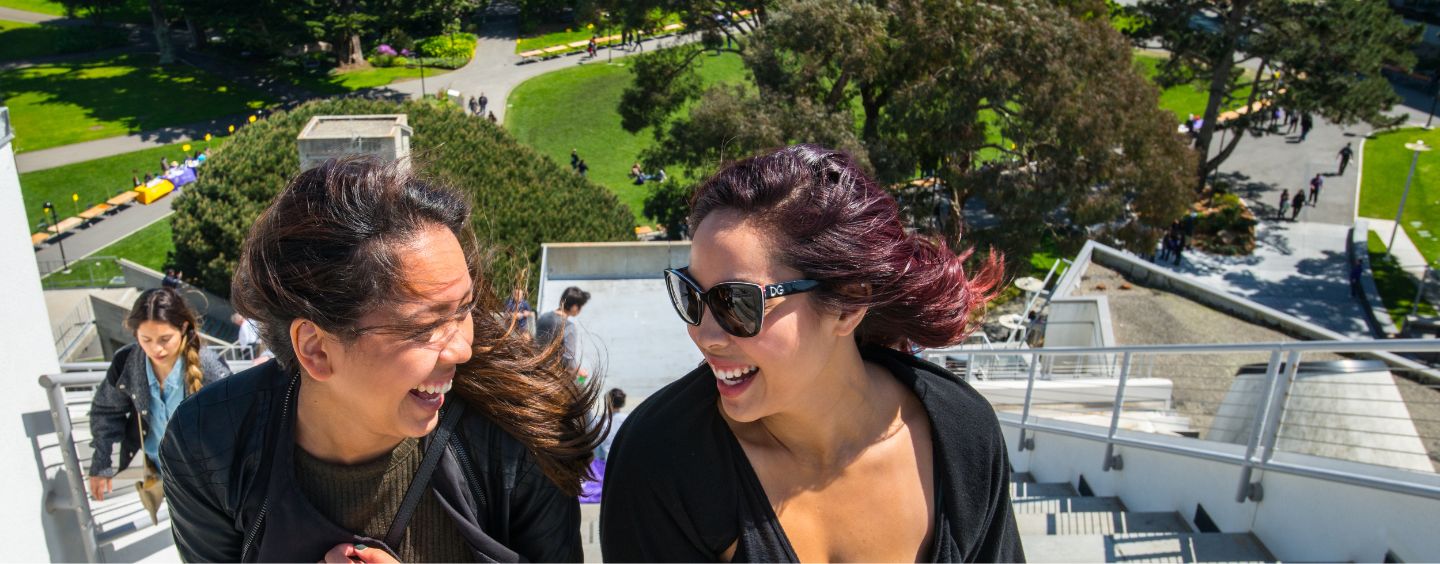 Two students with wind in their hair at the top of the steps above the Student Center