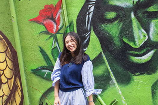 International student in front of a mural of Tupac Shakur