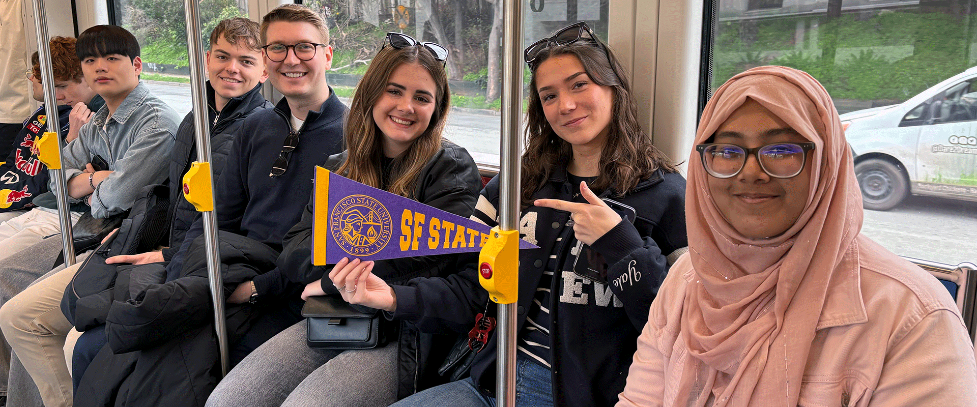 International students riding Muni metro, holding SFSU pennant