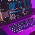 Laptop connected with code on screen connected to sound system, bathed in purple light