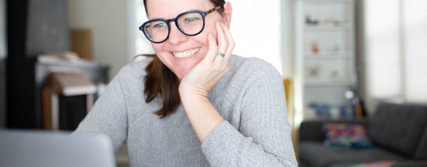 Instructional designer taking an online course, smiles while looking at laptop