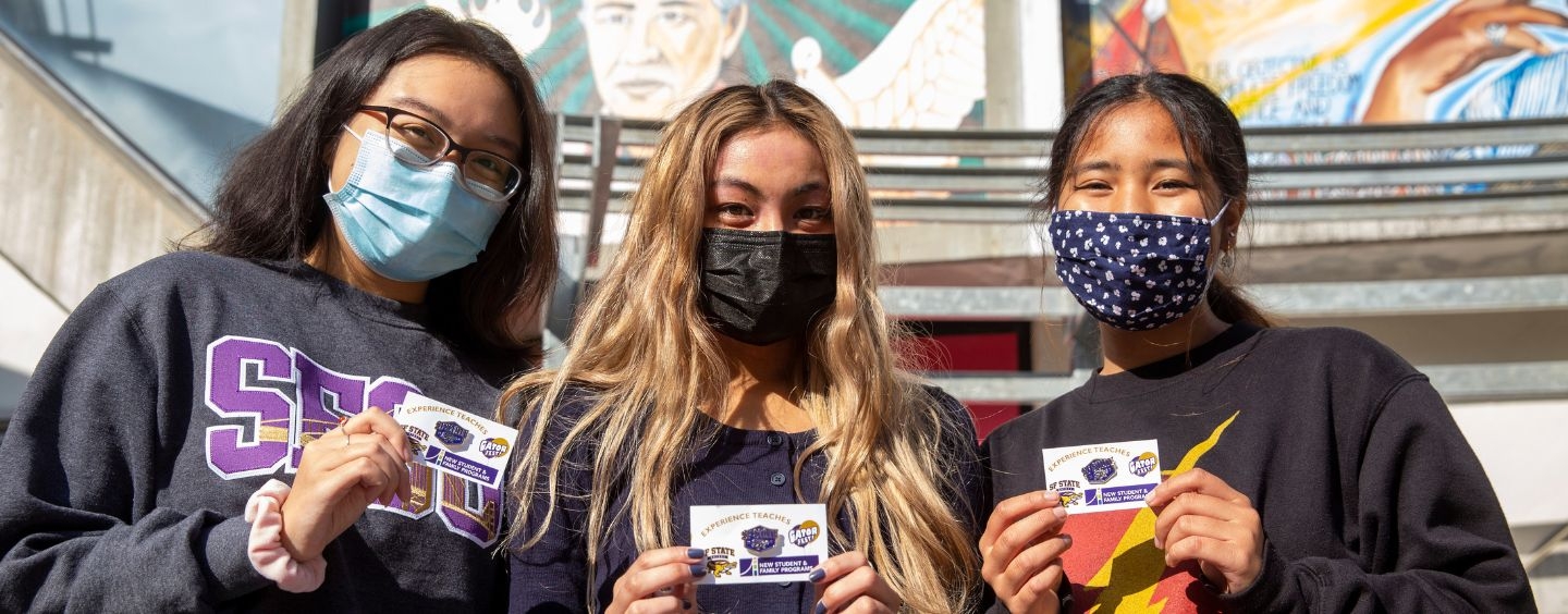 Three students in masks show their Gator Fest cards