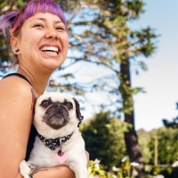 Student with purple hair holding a pug dog on campus