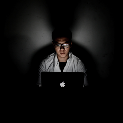 Hacker working in the dark with his face lit by a laptop screen.