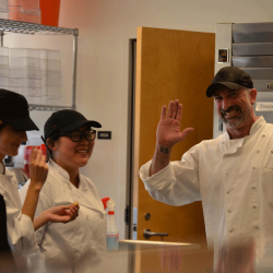 Chef teacher and kitchen staff students wave in the kitchen