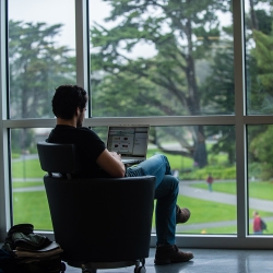 Student taking online class in the library, with a view of campus