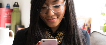 Mobile app developer smiles while looking at her pink smart phone