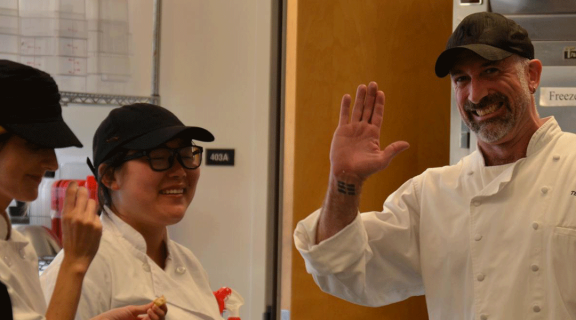 Chef teacher and kitchen staff students wave in the kitchen
