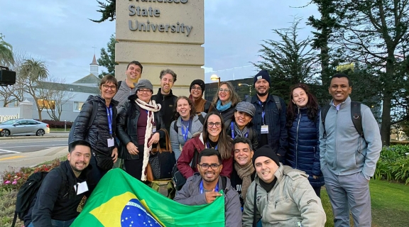 Teacher trainees hold a Brazilian flag in front of the SF State sign